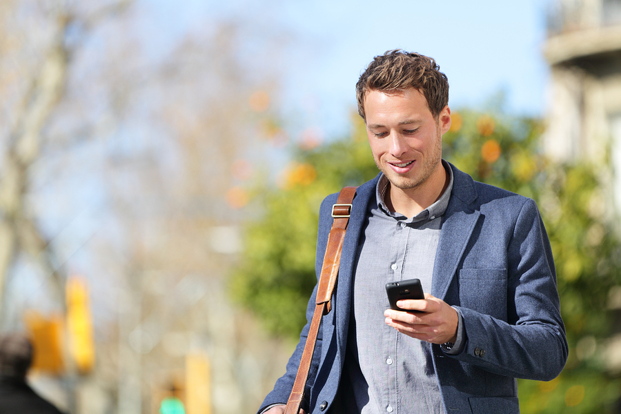 Young urban businessman professional on smartphone walking in st